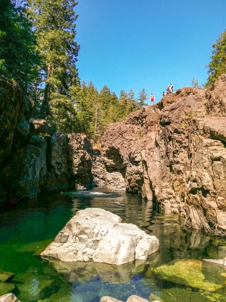 A view of the cliffs with people cliff jumping into the Sooke Potholes on Vancouver Island